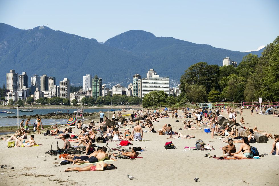 People relaxing on the sand of a beach with Vancouver skyline behind them and mountains in the background. 