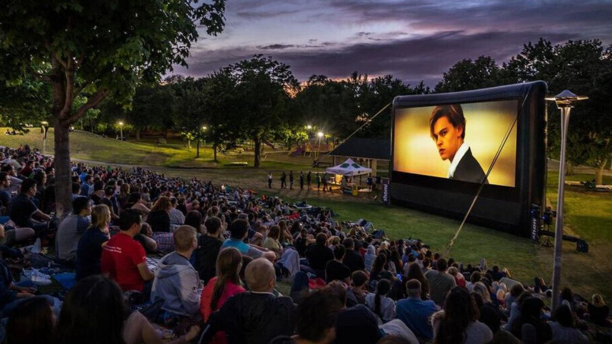 People sitting in a Toronto park watching an outdoor film at night.