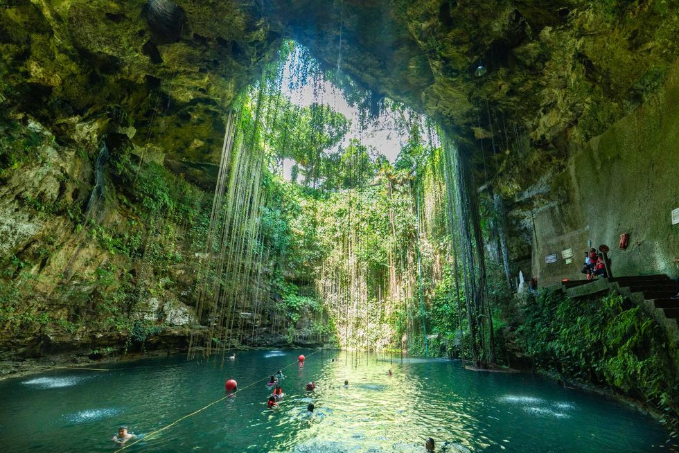 People swimming in the teal water of Ik Kil Cenote, the walls of which are covered in hanging vines.
