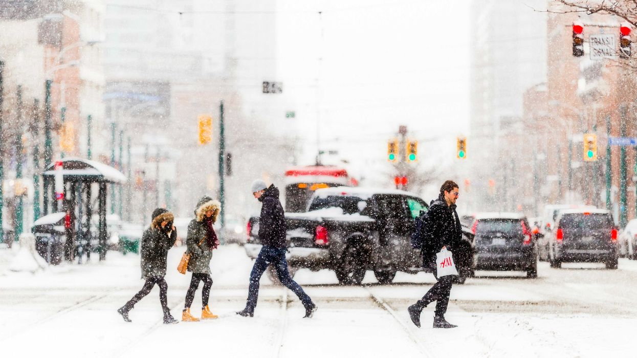 people walking across a street in toronto in front of cars while it snows