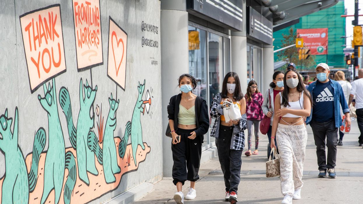 People walking on the sidewalk in Toronto are wearing face masks.