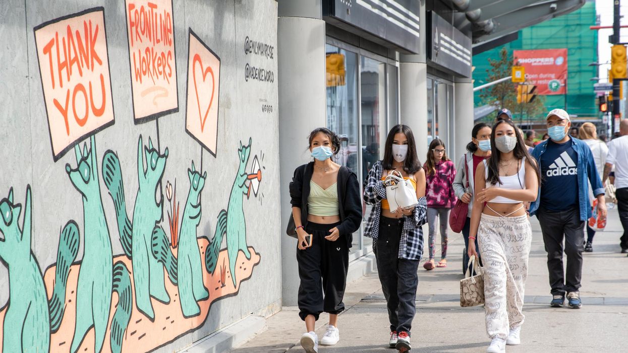 People walking on the sidewalk in Toronto are wearing face masks.