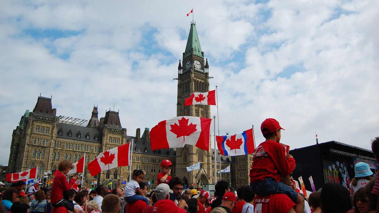 People wearing red and waving Canadian flags in front of Parliament Hill in Ottawa.