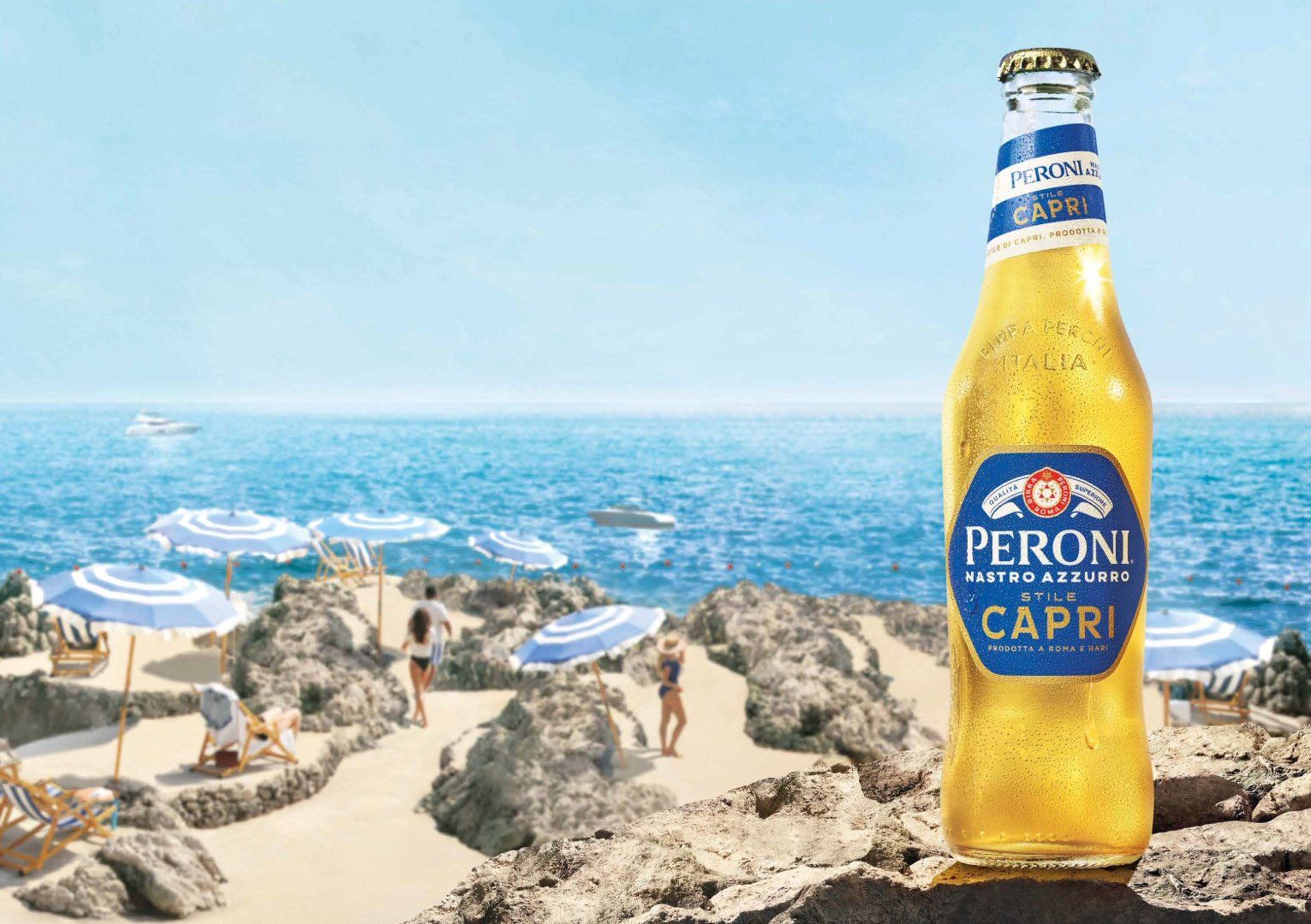 Peroni Capri beer on a sunlit coastal ledge with a Mediterranean beach scene in the background.