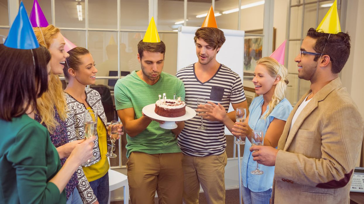 Person blowing on a cake's candles at an office birthday.