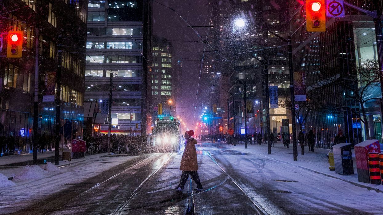 person crossing a street in toronto in front of a street car as it snows
