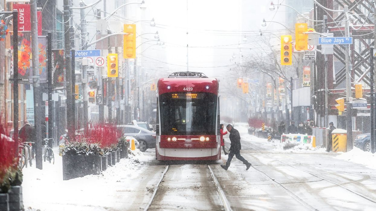 person crossing toronto street in front of ttc streetcar as it snows
