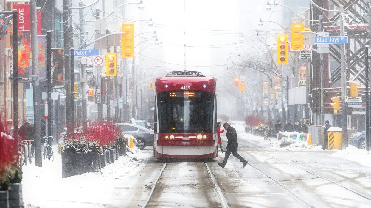 person crossing toronto street in front of ttc streetcar as it snows