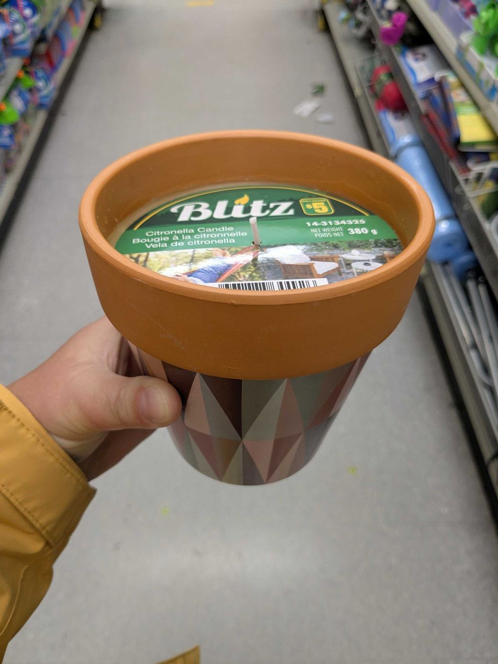 Person holding a citronella candle in an aisle in Dollarama