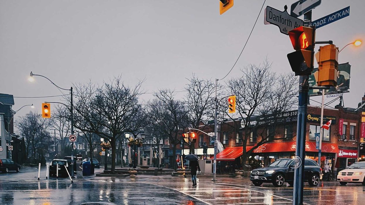 person holding an umbrella crossing a street in toronto as it rains