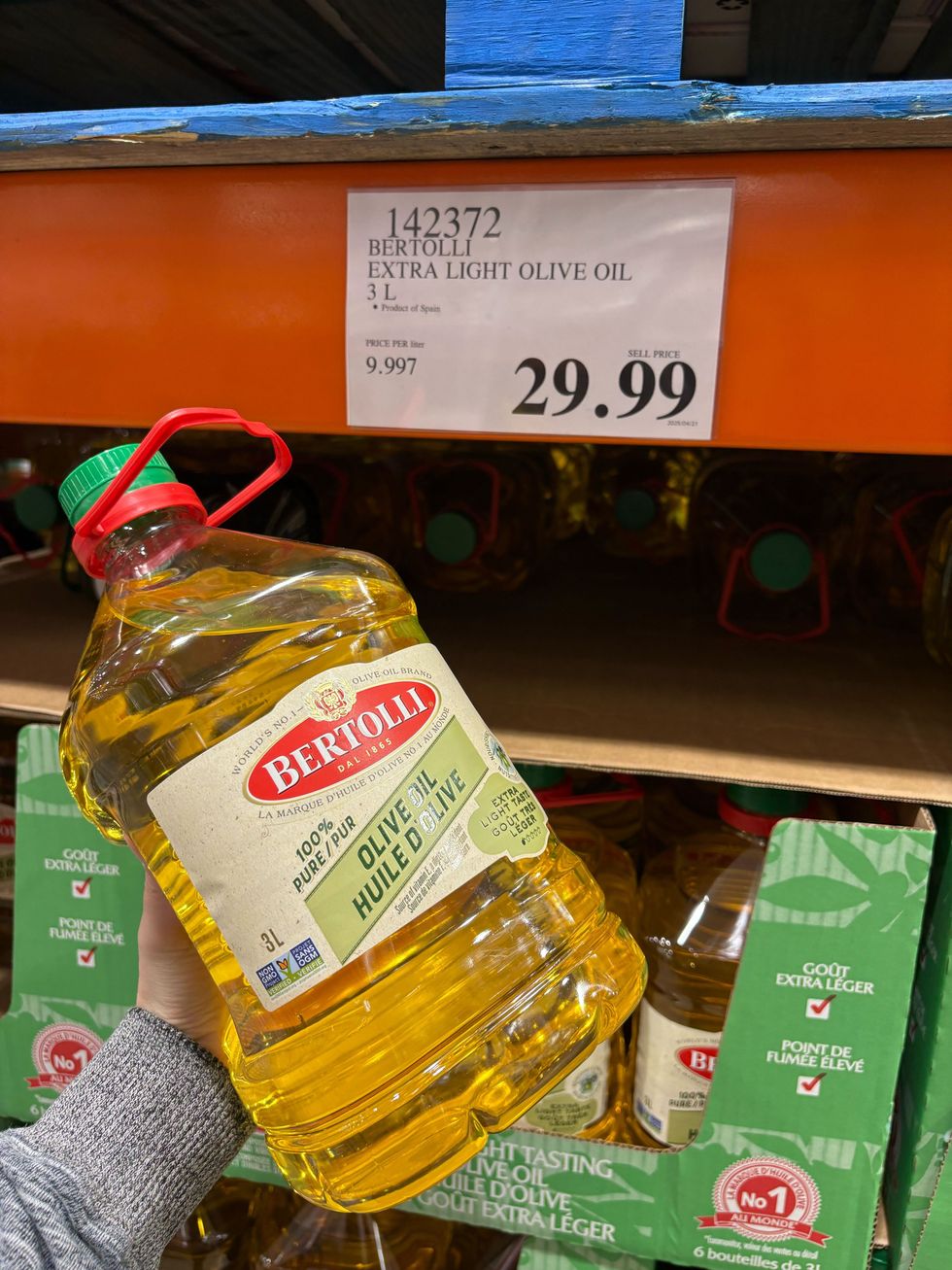 person holding bottle of bertolli olive oil at costco