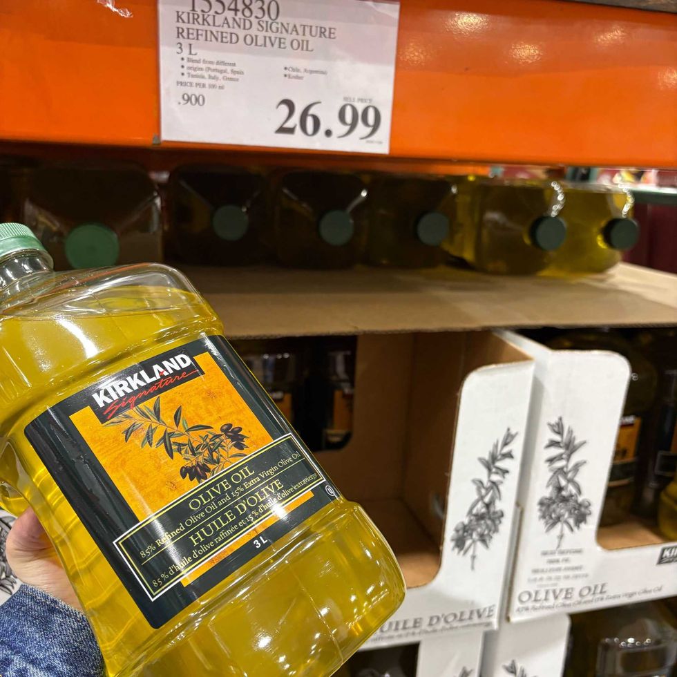 person holding bottle of kirkland signature light olive oil at costco