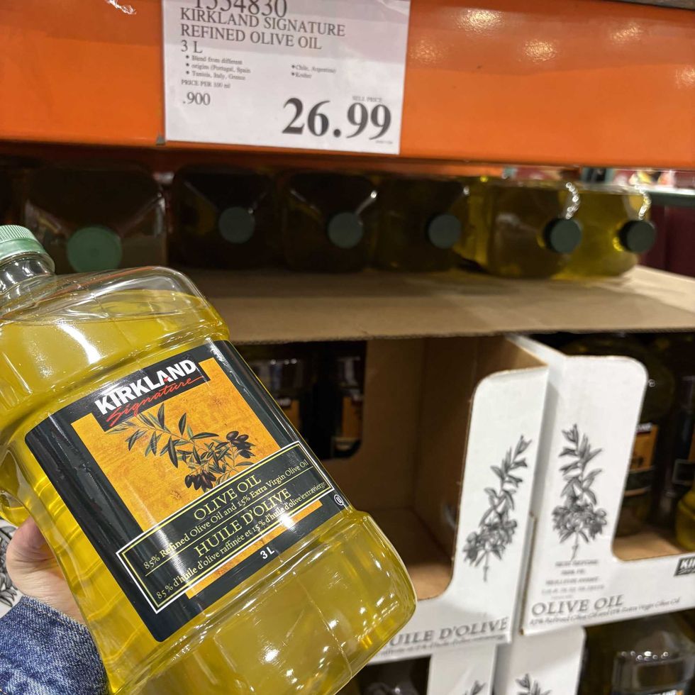 person holding bottle of \u200bKirkland Signature light olive oil at costco