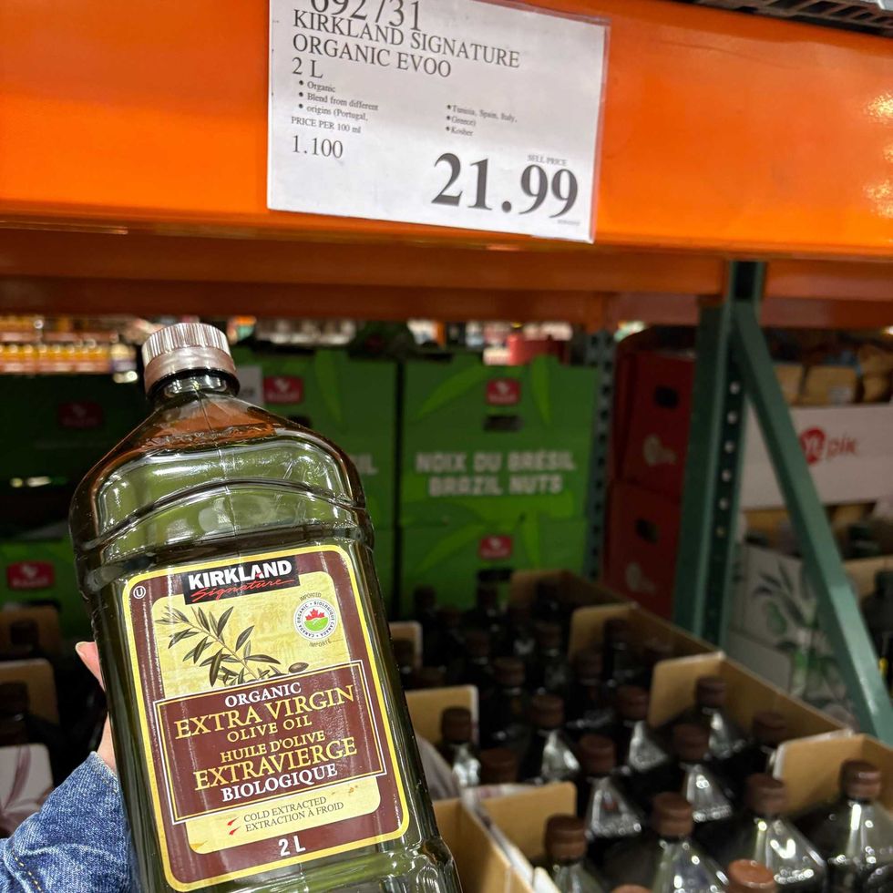 person holding bottle of \u200bKirkland Signature olive oil at costco