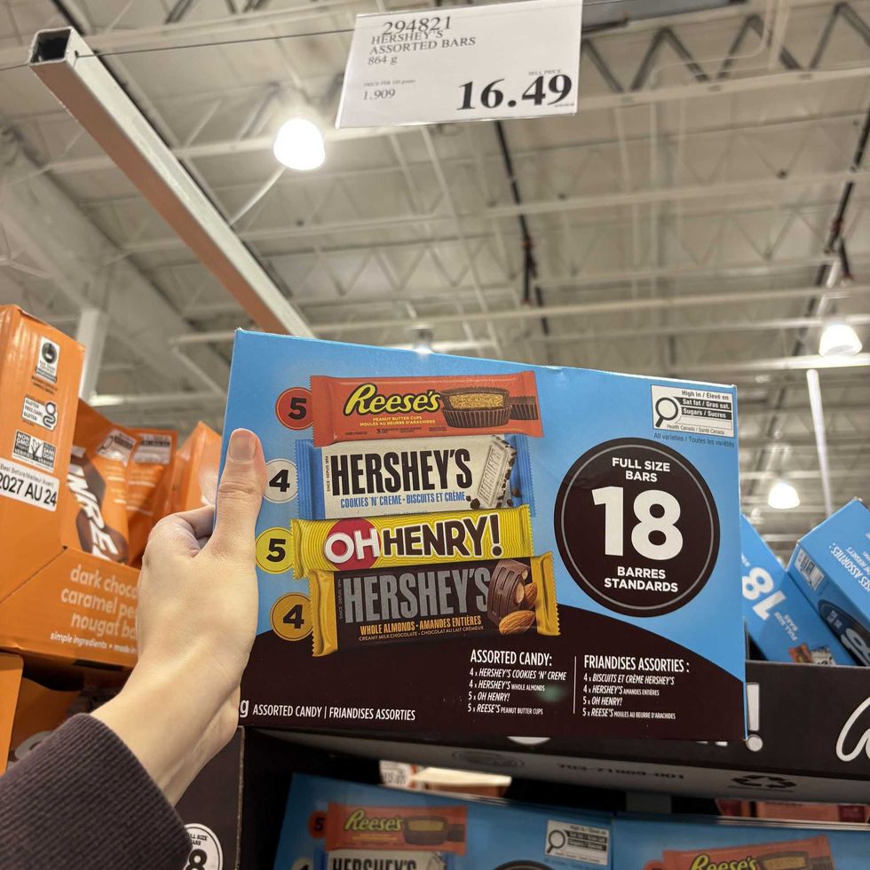 person holding box of Reese's, Hershey's Cookies 'n' Creme, Oh Henry and almond Hershey's at Costco