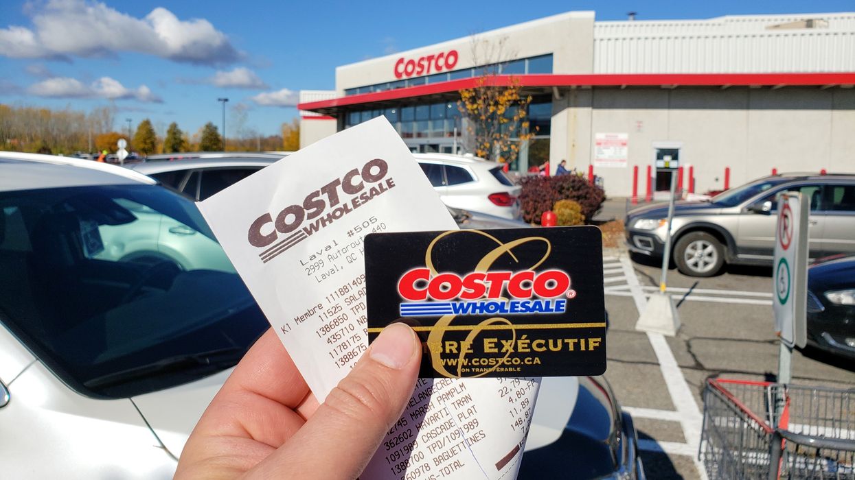 person holding costco membership card and receipt in front of a costco store