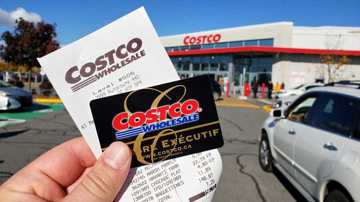 person holding costco membership card and receipt in front of costco store in canada