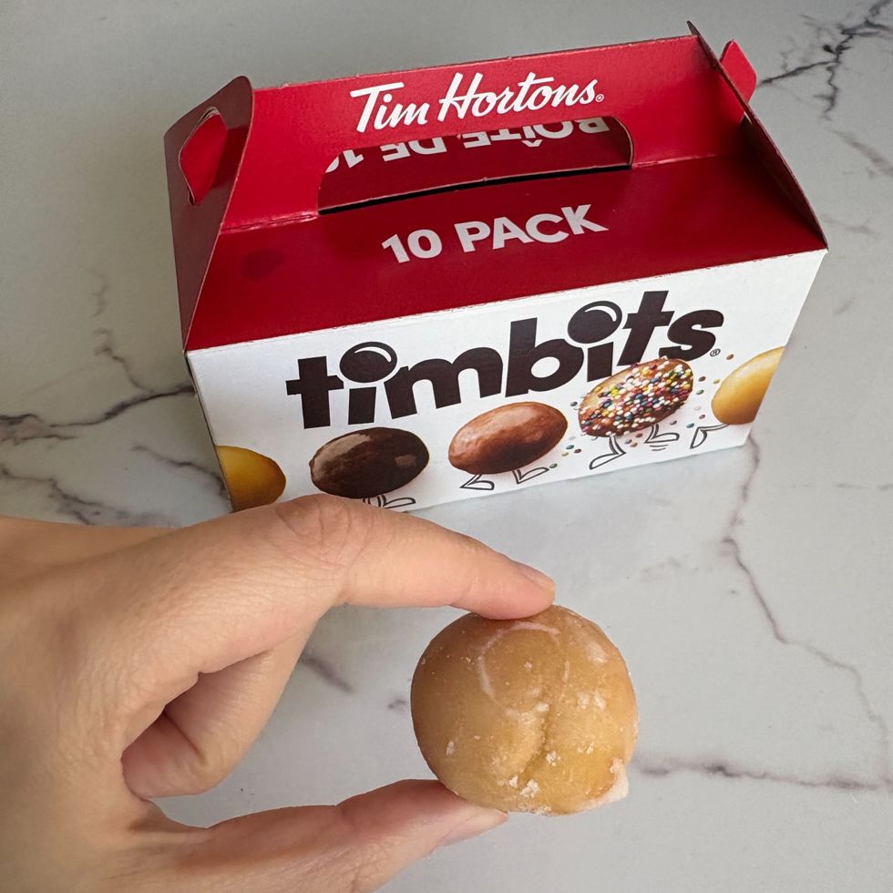 person holding honey dip timbit in front of timbits box from tim hortons