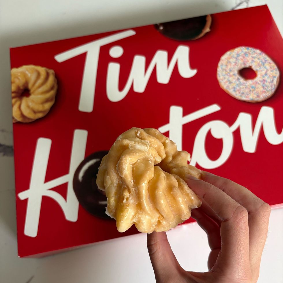 person holding tim hortons honey cruller donut