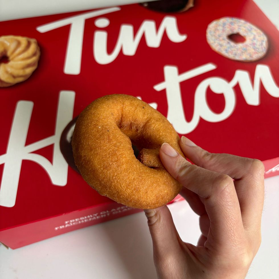 person holding tim hortons old fashioned plain donut