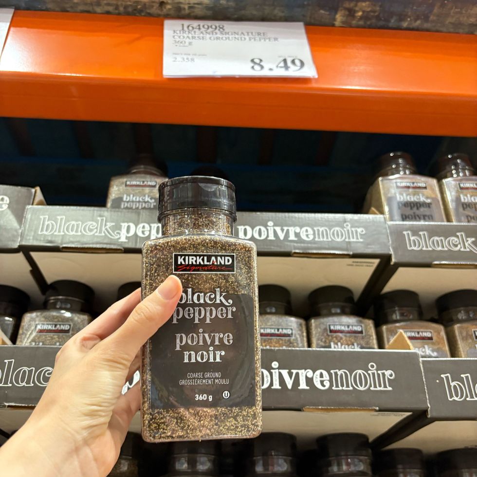 person holding tub of Kirkland Signature ground black pepper