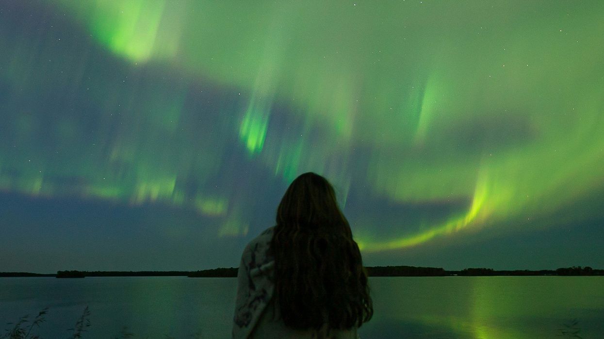 person looking at northern lights in the sky over a lake in saskatchewan