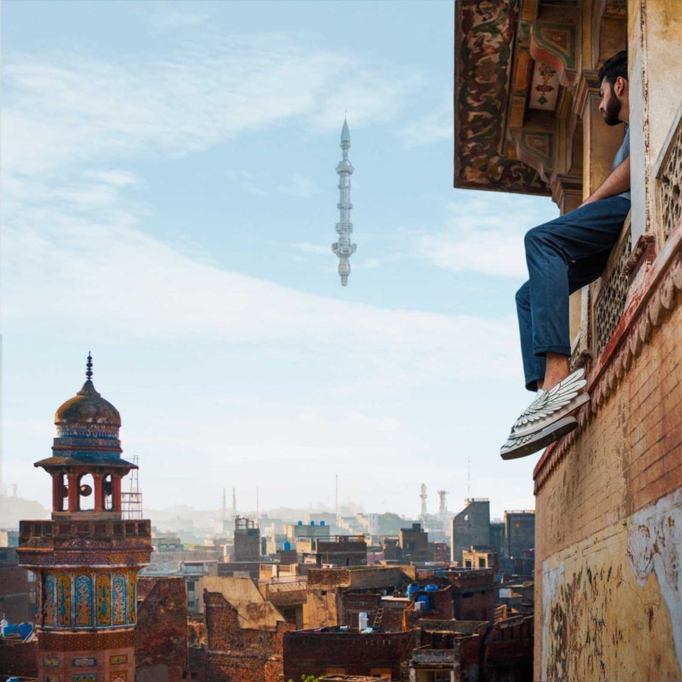 Person seated on a ledge, cityscape and floating tower in the background.