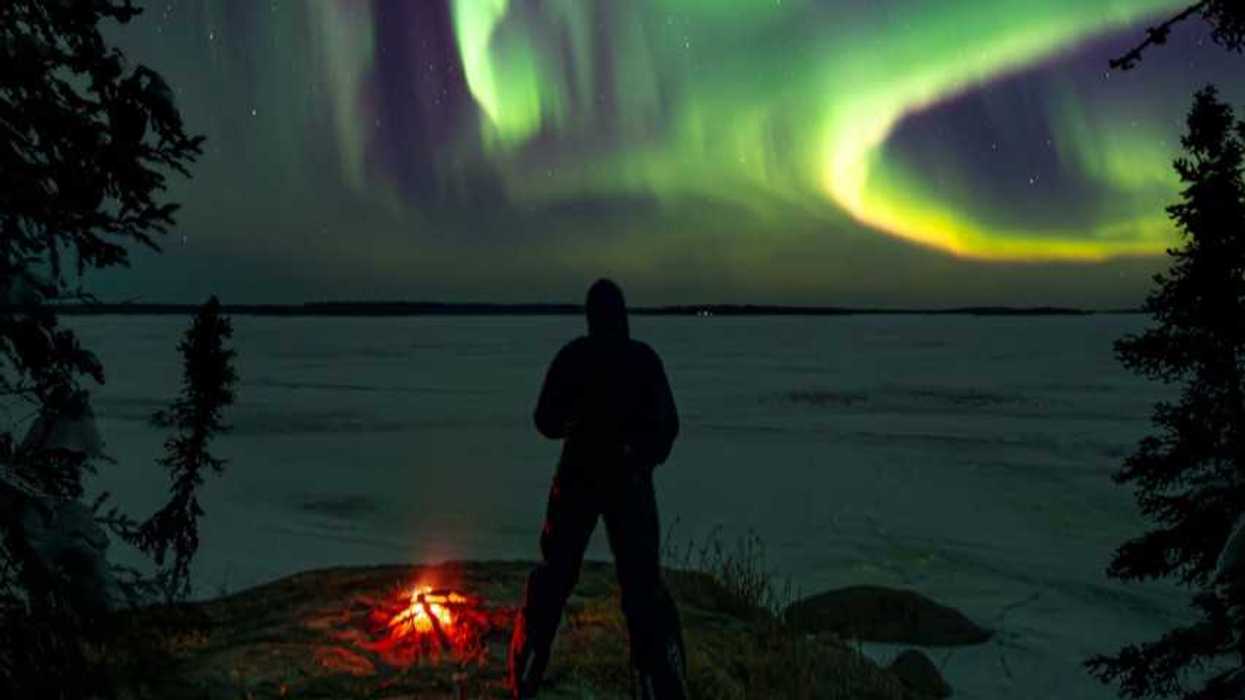 person standing near lake looking at green northern lights in sky