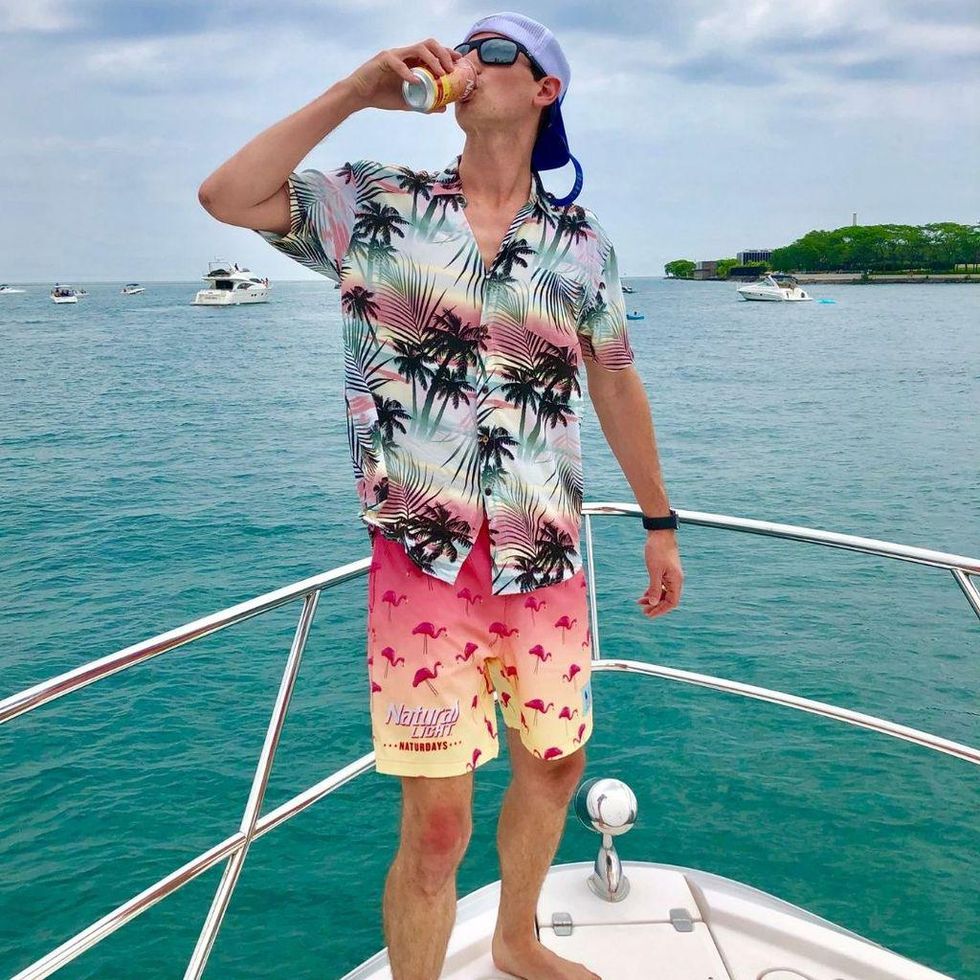 person standing on a boat in the water drinking from a can with the shirt on