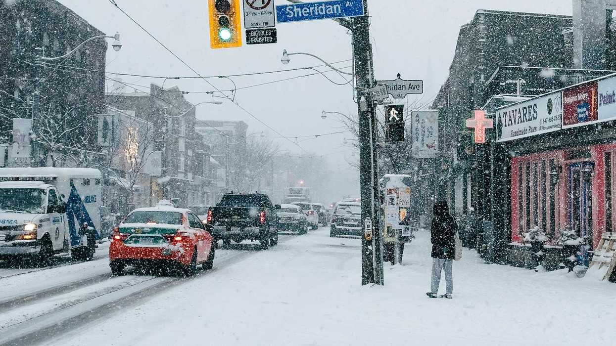 person standing on sidewalk as cars go by on toronto street during snowstorm