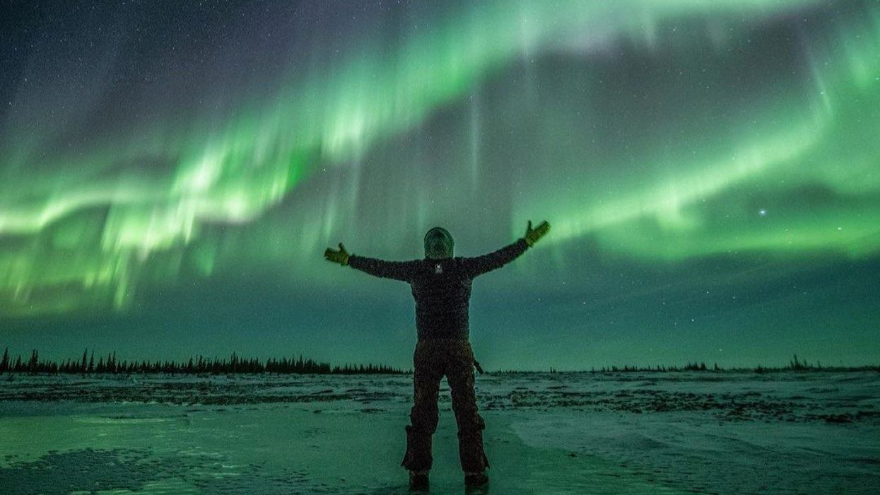 person standing with their arms outstretched and green northern lights in the sky behind them in churchill, manitoba