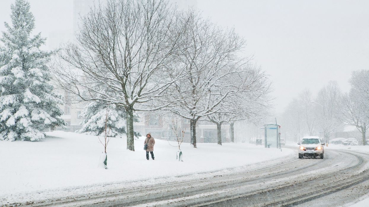 person walking on sidewalk and car driving on street in toronto during snowstorm