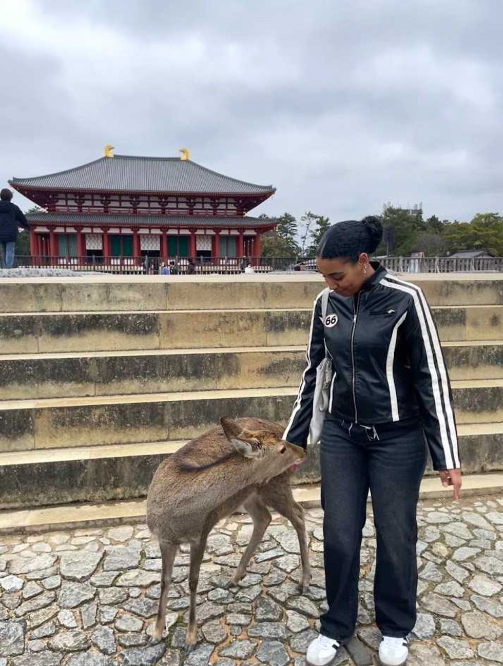 Person wearing a black-and-white leather jacket while petting a deer at a temple in Nara, Japan.