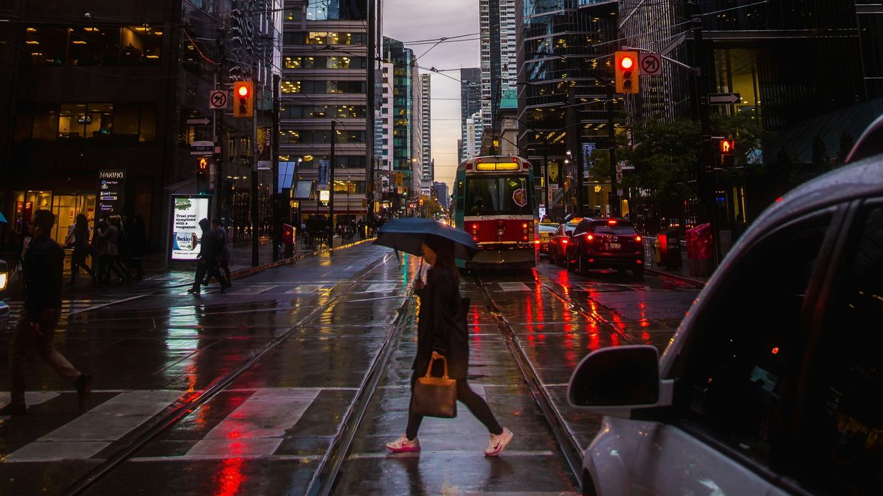 person with an umbrella walking across a toronto street as it rains