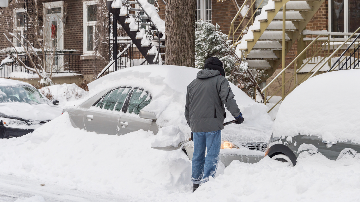 Personne qui déneige sa voiture enterrée par la neige avec une pelle sur une rue de Montréal.