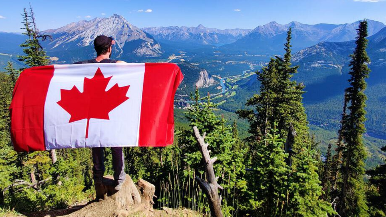 Personne tenant un drapeau canadien sur le bord d'une falaise avec vue sur les Rocheuses.
