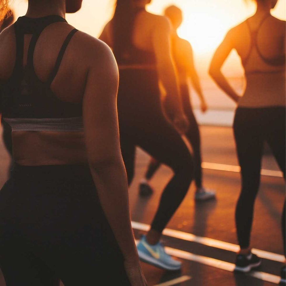 Personnes participant \u00e0 un cours de fitness en plein air au coucher du soleil.