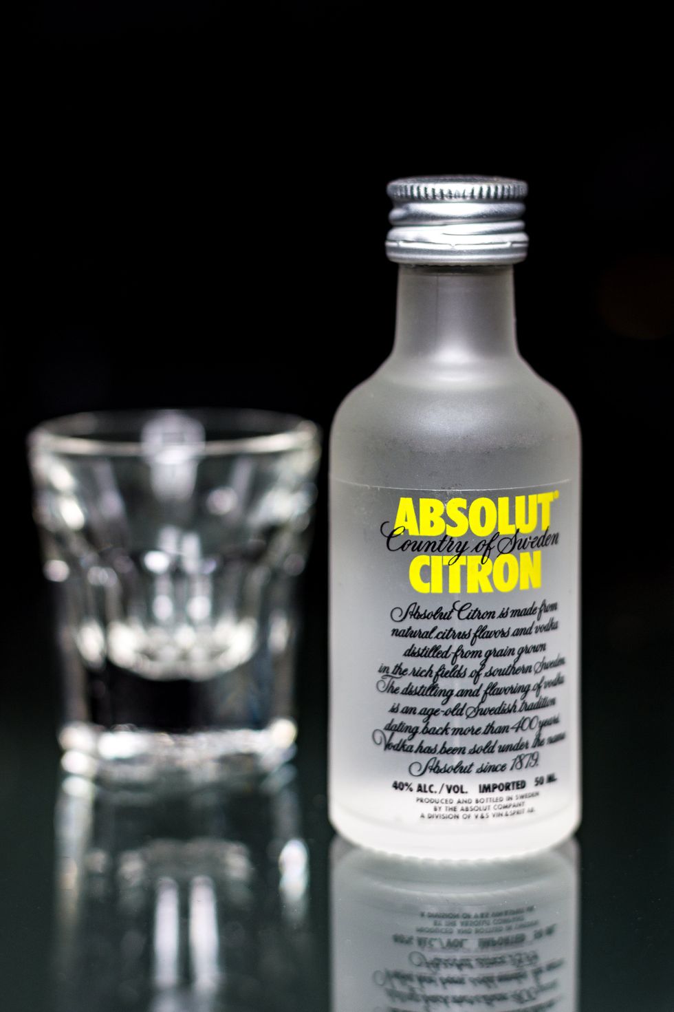 Petite bouteille de vodka Absolut au citron avec un shooter en arri\u00e8re-plan.