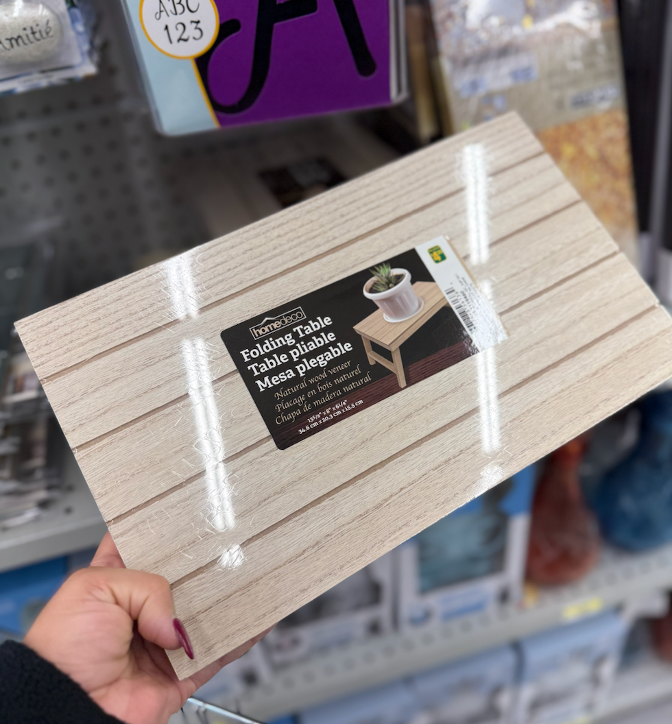 Petite table pliante en placage de bois naturel tenue en main dans une all\u00e9e du Dollarama.