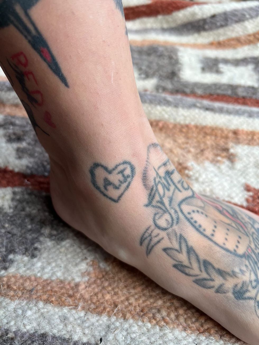 Pied avec tattoos des initiales A. J. sur un tapis color\u00e9.