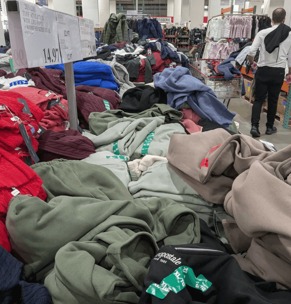 Piles of clothing on a store table with various colors and a price sign overhead.