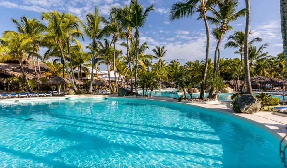 Piscine d'un h\u00f4tel entour\u00e9e de chaises longues et de palmiers.