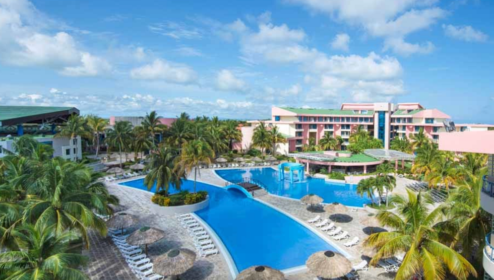 Piscine d'un h\u00f4tel entour\u00e9e de chaises longues et de palmiers.