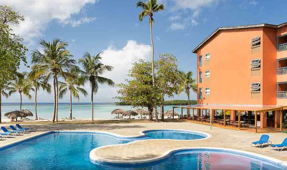 Piscine d'un h\u00f4tel entour\u00e9e de chaises longues et de palmiers.