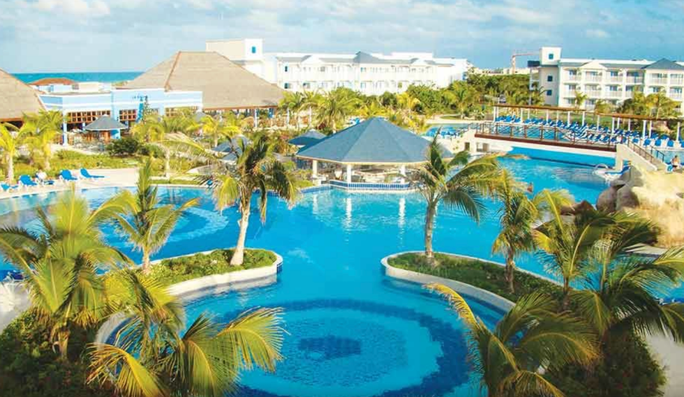 Piscine d'un h\u00f4tel entour\u00e9e de chaises longues et de palmiers.