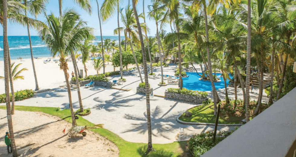 Piscine et plage bord\u00e9es de palmiers au Coral Costa Caribe Resort en R\u00e9publique dominicaine