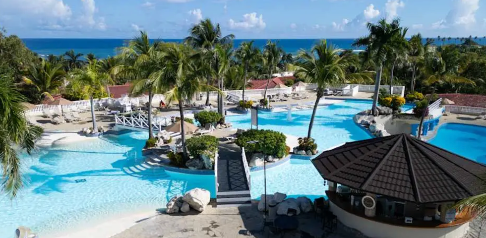 Piscines en forme de lagon entour\u00e9es de palmiers, de ponts et d\u2019espaces d\u00e9tente, avec vue sur l\u2019oc\u00e9an au Cofresi Palm Beach Resort and Spa.