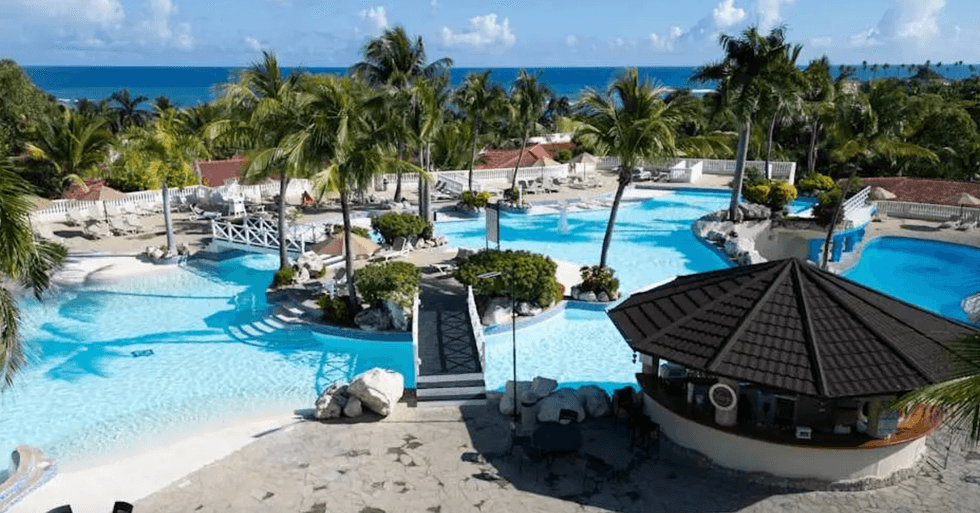 Piscines lagon turquoise entour\u00e9es de palmiers avec passerelles et zones de d\u00e9tente au bord de la mer dans un resort tout inclus.