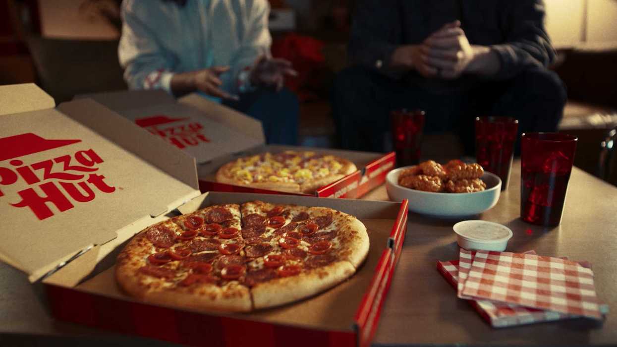 Pizza Hut boxes open on a coffee table with napkins, wings and dip.