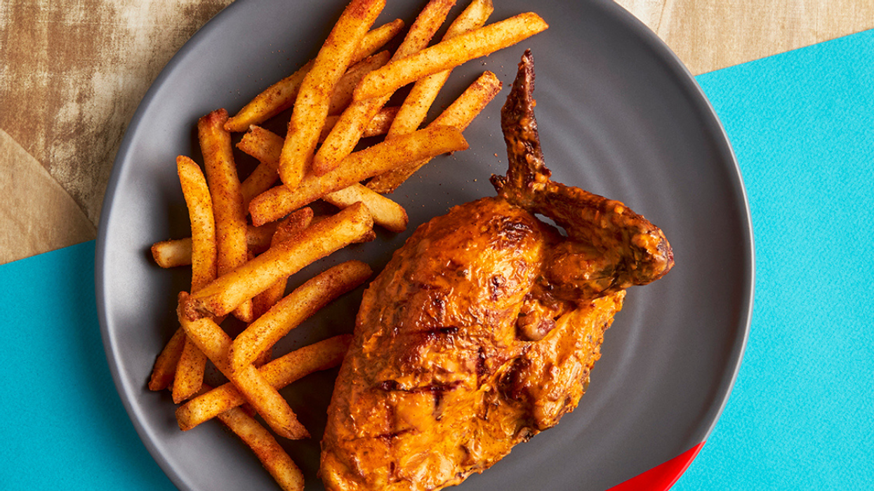 Plate of seasoned French fries served with a piece of spicy roasted chicken on a dark grey dish.